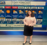 Elizabeth Temple standing in front of a weather broadcast smiling